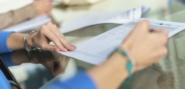 Γυνάικα συμπληρώνει έντυπο για Ταξινόμηση Οχήματος σε γραφείο, με έντυπα και στυλό πάνω σε γυάλινο τραπέζι.